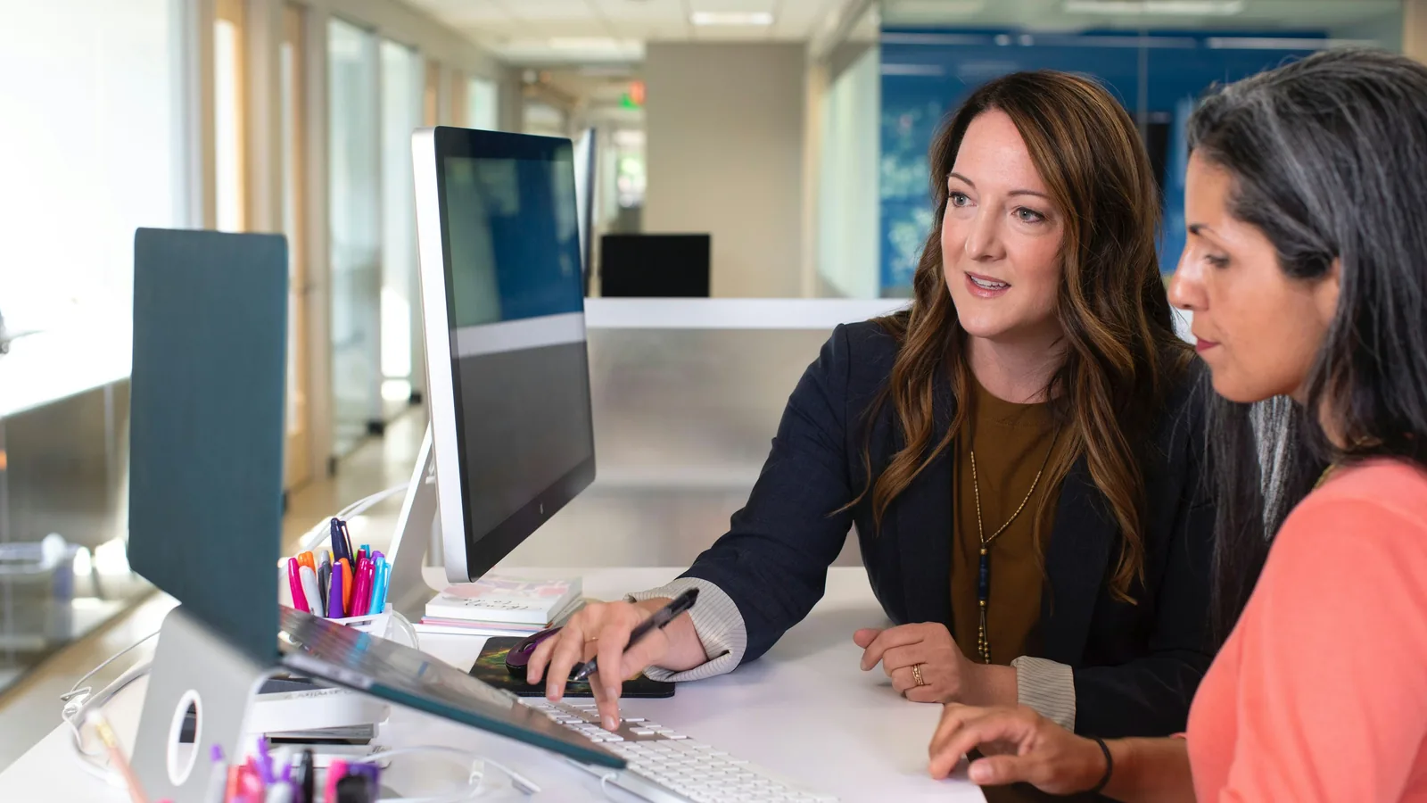 One colleague leaning over another's screen to explain something