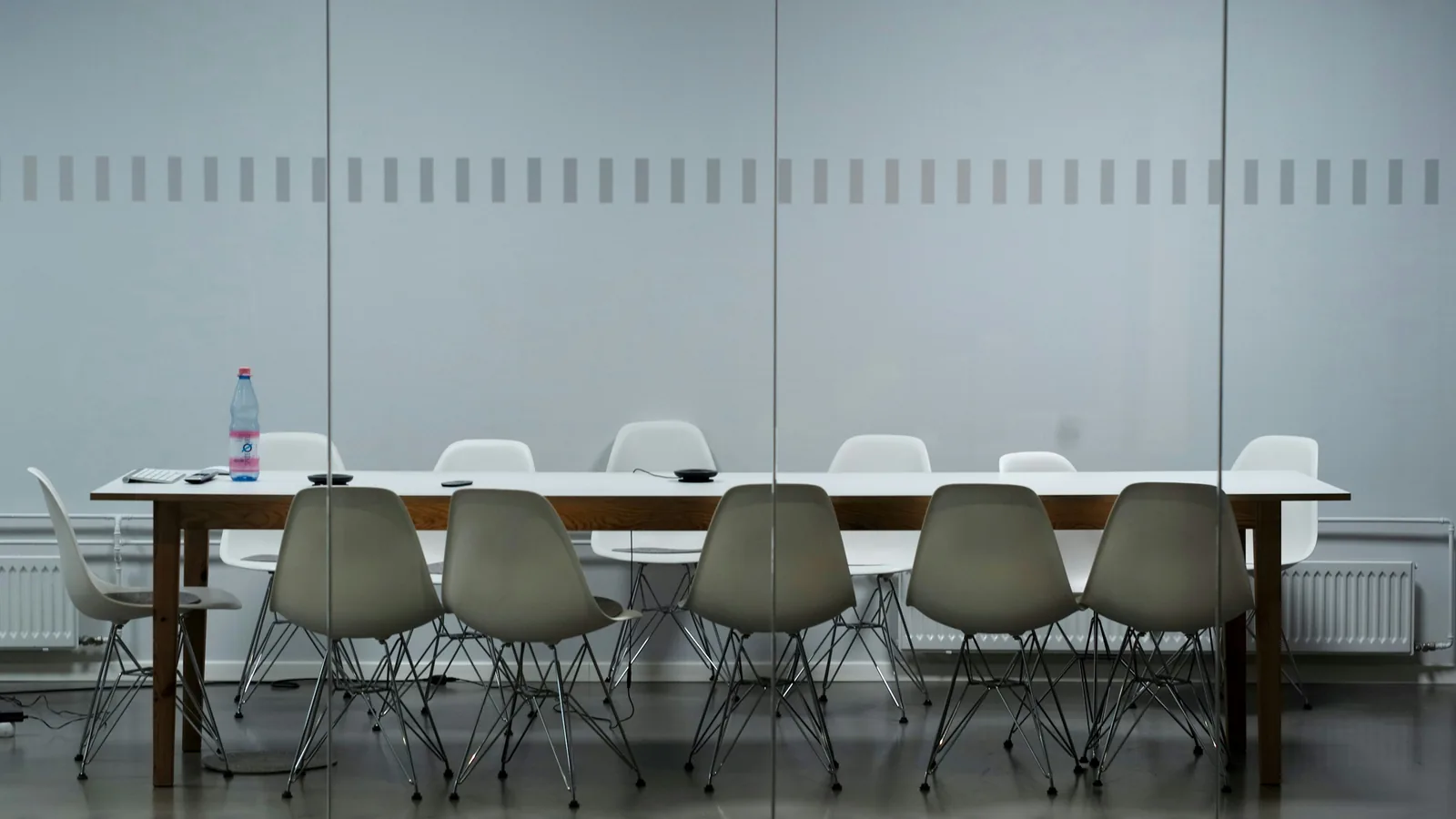An empty meeting room, no one at the chairs, one bottle left on the table