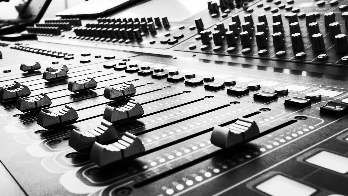 A mixing console with many faders and knobs, in black and white