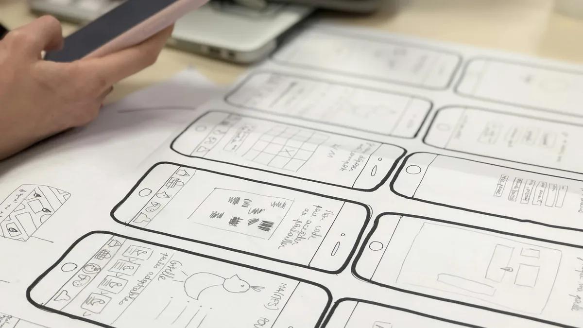 Hand drawn screen sketches on paper with a phone beside them