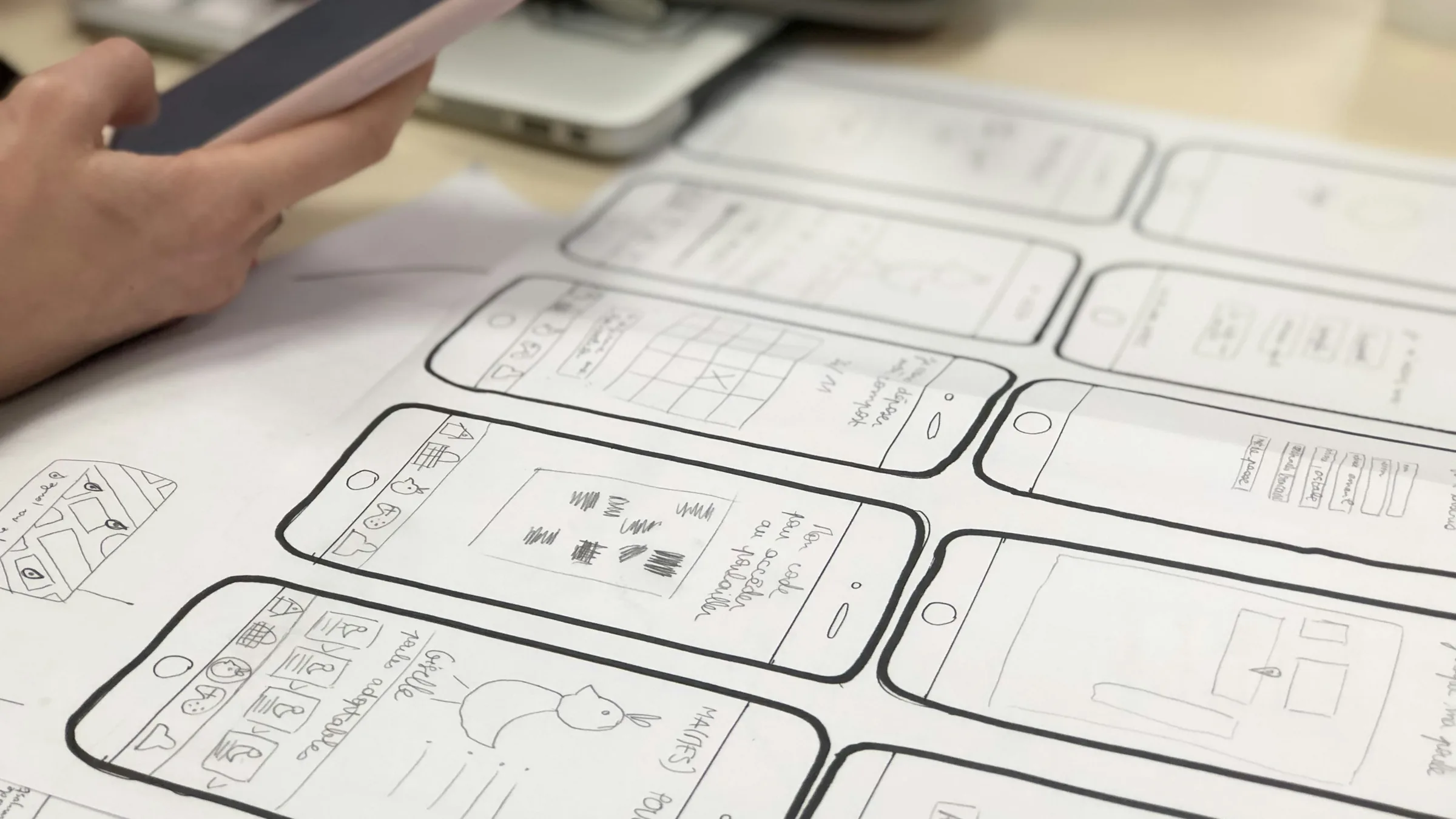 Hand drawn screen sketches on paper with a phone beside them