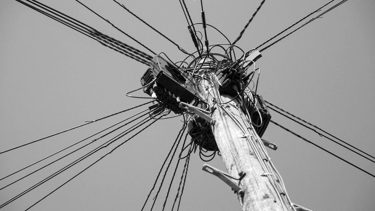 A tangle of wires at the top of a pole against a plain sky