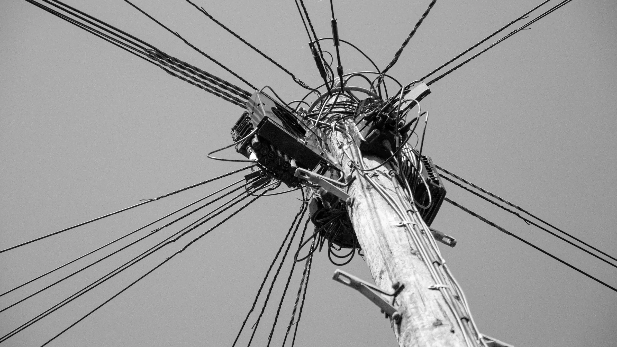 A tangle of wires at the top of a pole against a plain sky