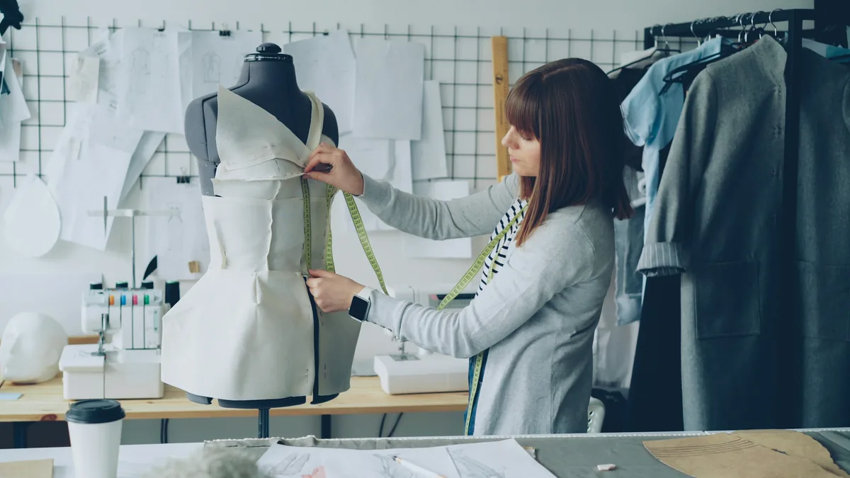 A dressmaker fitting a garment on a mannequin with a tape measure
