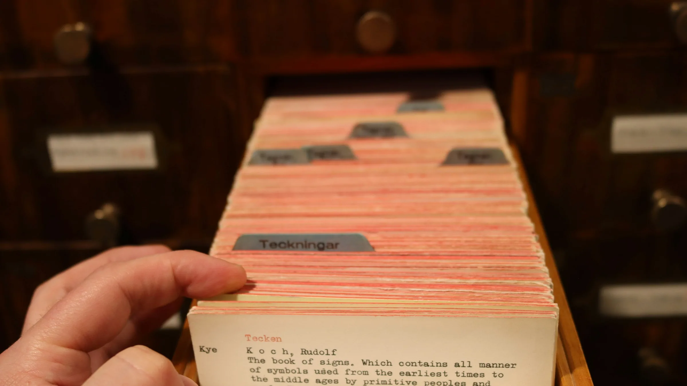 A hand lifting one card from a catalogue drawer, labelled dividers between the cards