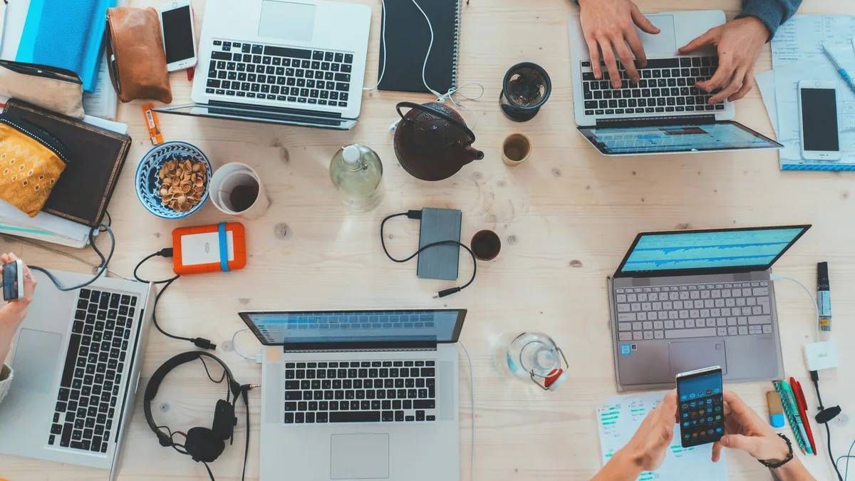 A table seen from above with four laptops, phones and headphones side by side